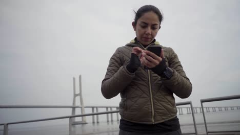 Thoughtful-brunette-lady-using-smartphone-at-seaside