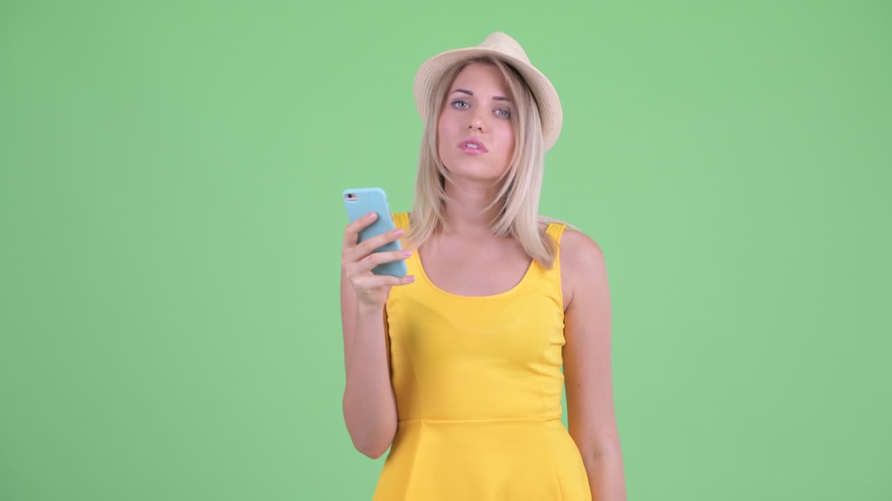 젊은 관광 여성이 녹색 배경에 휴대전화를 사용하면서 충격적인 소식을 듣는 스튜디오 촬영
