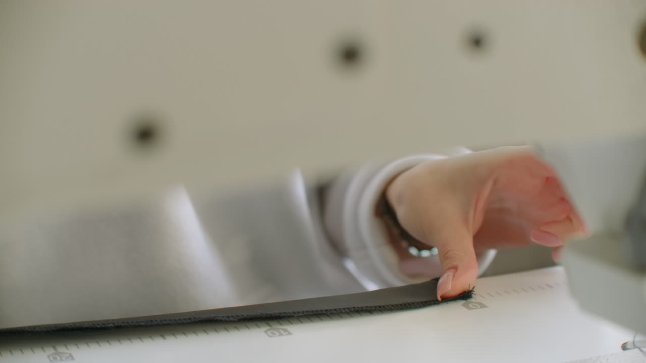 바느질기 바늘은 움직이고, 바느질기의 바늘은 빠르게 위아래로 움직이고, 매는 사람이 바느질 작업장에서 검은색 천을 는다.