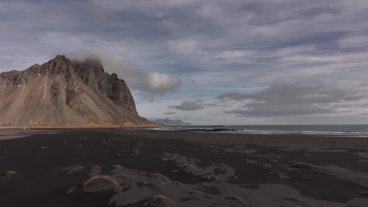 cloudy skies loom over black sand and rugged cliffs in Iceland