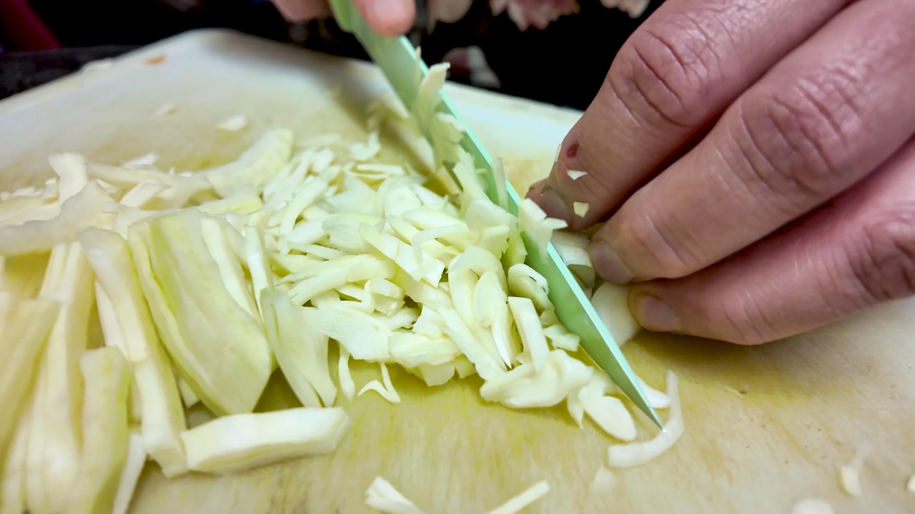 Hands slice cabbage on a wooden board, showcasing home cooking and food prep.