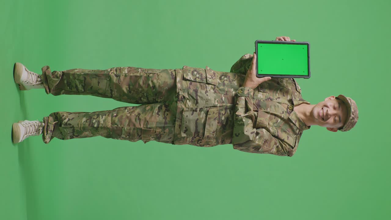Full Body Of Asian Man Soldier Smiling And Showing Green Screen Tablet To The Camera While Standing In The Green Screen Background Studio