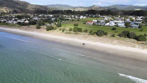 Aerial-View-of-Golf-Cart-Driving-On-The-Seashore-Of-Matarangi-Beach-In-Waikato,-New-Zealand