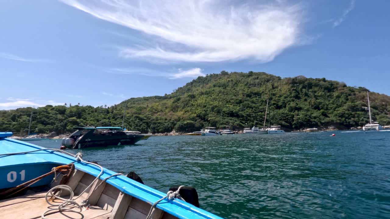 Blue wooden boat approaches lush green island on calm sea under bright daylight and clear sky