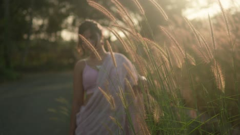 mujer en sari en medio de la hierba alta al atardecer, la luz dorada filtrando a través, evocando la serenidad