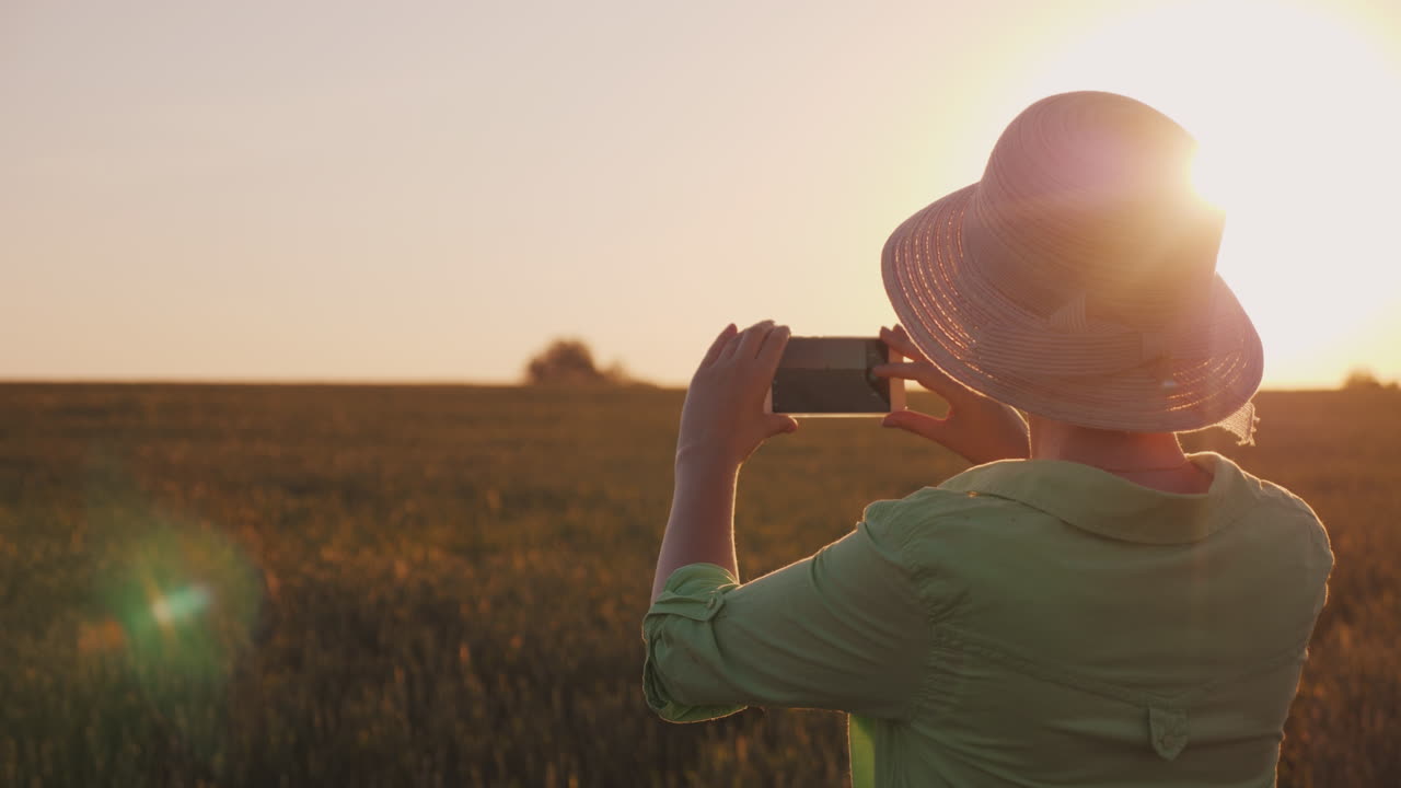 женщина в шляпе фотографирует красивый закат над пшеничным полем концепция органического земледелия 4