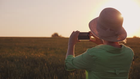 Eine-Frau-Mit-Hut-Fotografiert-Einen-Wunderschönen-Sonnenuntergang-über-Dem-Weizenfeld-Konzept-Des-ökologischen-Landbaus-4