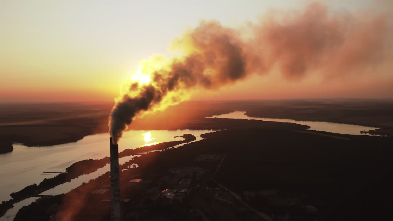Pipes pollute atmosphere with smoke against the setting sun. Ecology pollution. Smoke stacks emit from industry on the background of lakes at sunset.