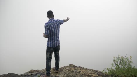 hombre africano parado al borde de un acantilado y mirando hacia una niebla nublada