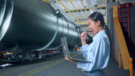 side view of happy asian business woman celebrating using laptop computer in pipe manufacturing factory