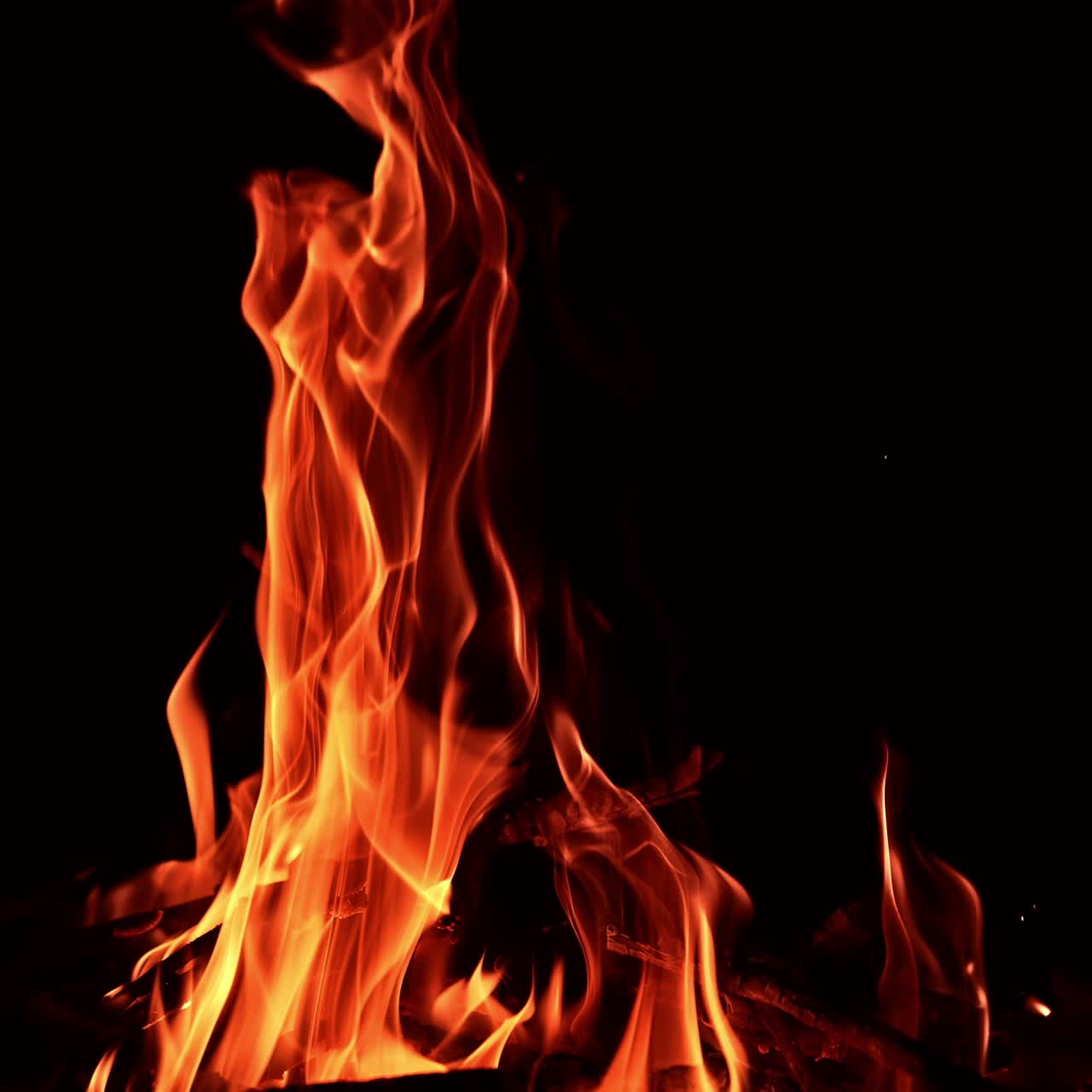 Dei bastoncini di legno bruciano nel fuoco. Fiamme arancioni e calde si estendono verso l'alto nell'aria. Sfondo nero
