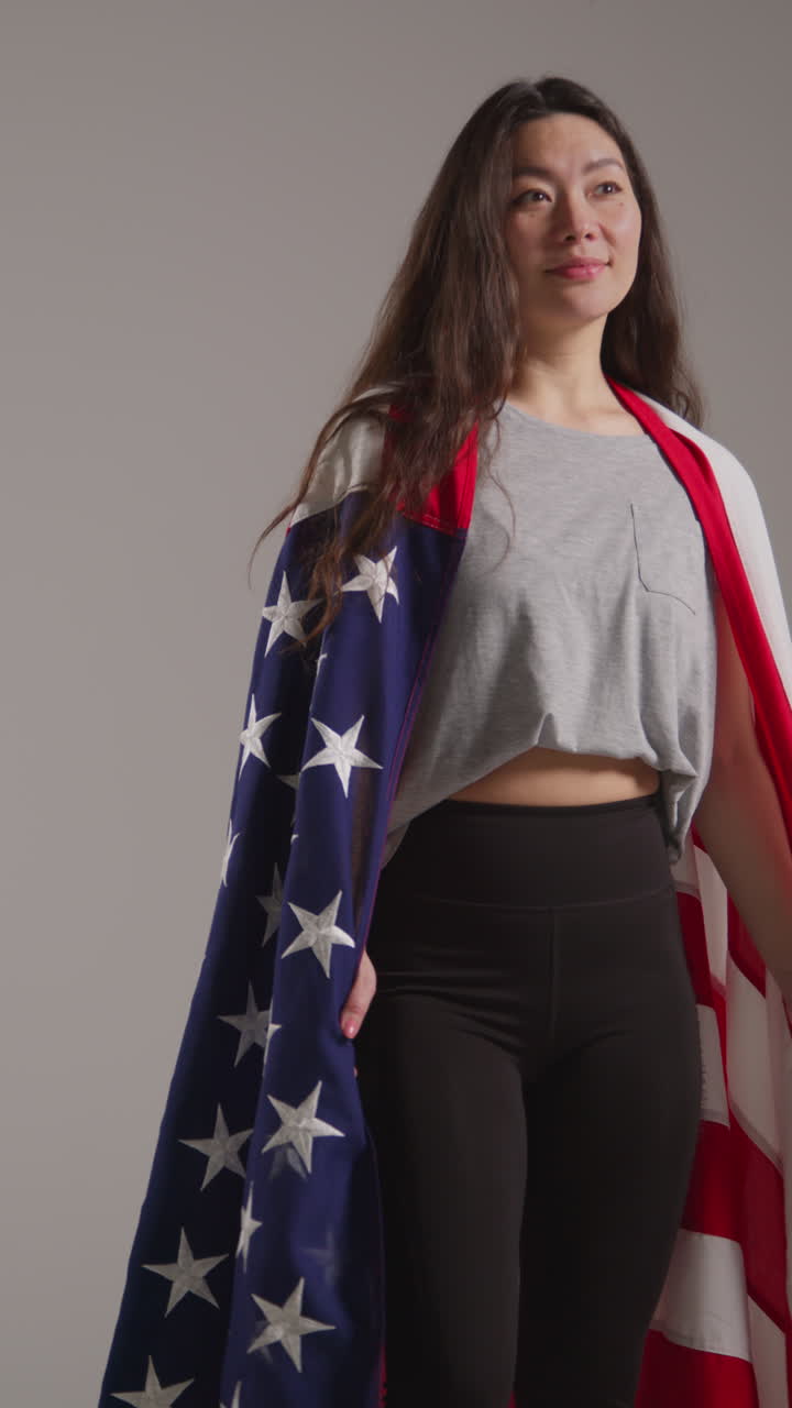 video de estudio vertical de una mujer envuelta en la bandera estadounidense celebrando el 4 de julio, día de la independencia