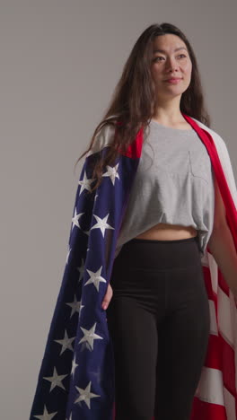 Toma-De-Estudio-De-Video-Vertical-De-Una-Mujer-Envuelta-En-La-Bandera-Estadounidense-Celebrando-El-4-De-Julio,-Día-De-La-Independencia