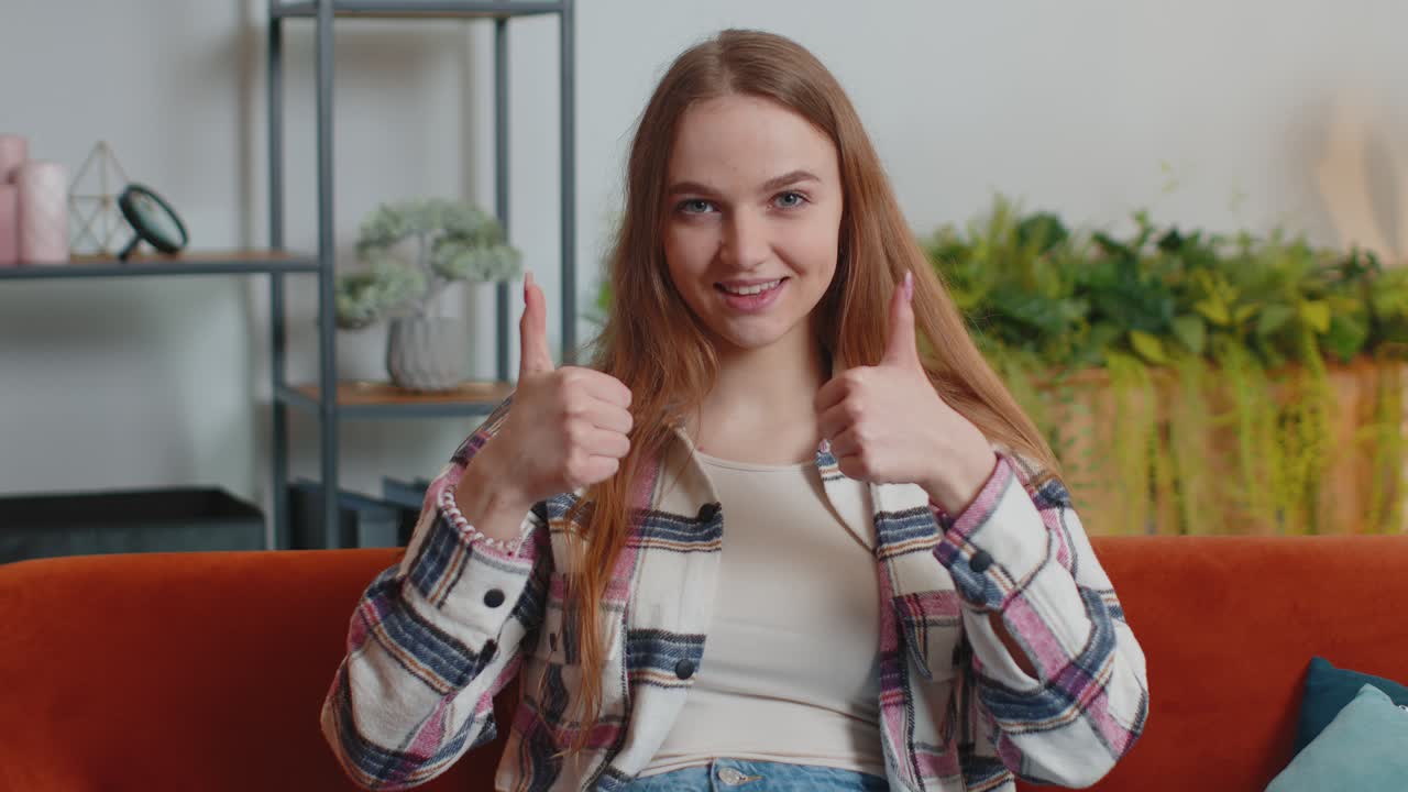 joven bonita mirando a la cámara levanta los pulgares está de acuerdo con algo positivo bueno en casa