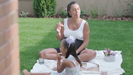 a mother and her young daughter sit on a blanket in the backyard, engaging in a drawing activity together. the outdoor scene captures a peaceful family moment, fostering creativity and bonding.