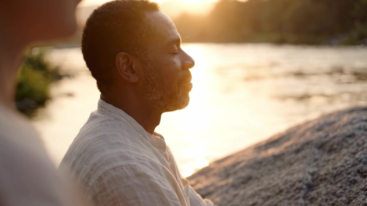 Um momento de paz à beira-rio, capturando tranquilidade e atenção plena enquanto dois indivíduos meditam juntos ao pôr do sol, abraçando a beleza e a serenidade da natureza