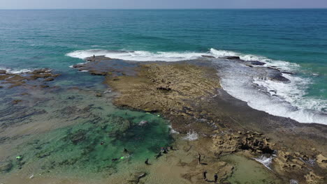 descending, tilting aerial to tourists snorkeling on rocky ocean point