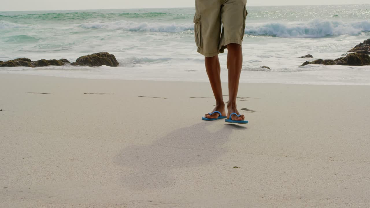 Nederste del af mand, der går barfodet på stranden en solrig dag 4k