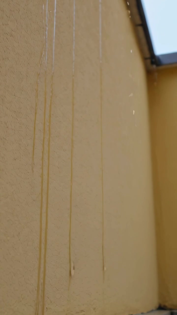 Vertikal video: Dryppende vandstriber løber ned ad en gul stukvæg, mens det begynder at småregne, med plads til tekst.