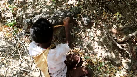 Un-Joven-Miembro-De-La-Tribu-Hadzabe-Pelando-La-Raíz-De-Baobab-Para-Comer-En-Un-Entorno-Forestal