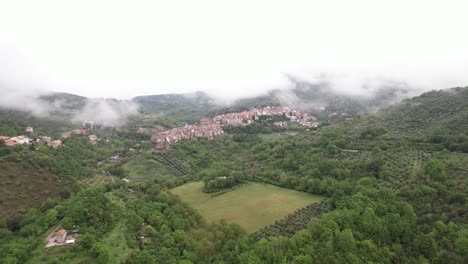 Aerial-over-a-lush-green-valley-toward-small-Italian-village