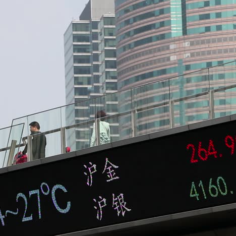 Chinese-business-people-walk-across-a-bridge-with-the--Hang-Seng-stock-market-index-below