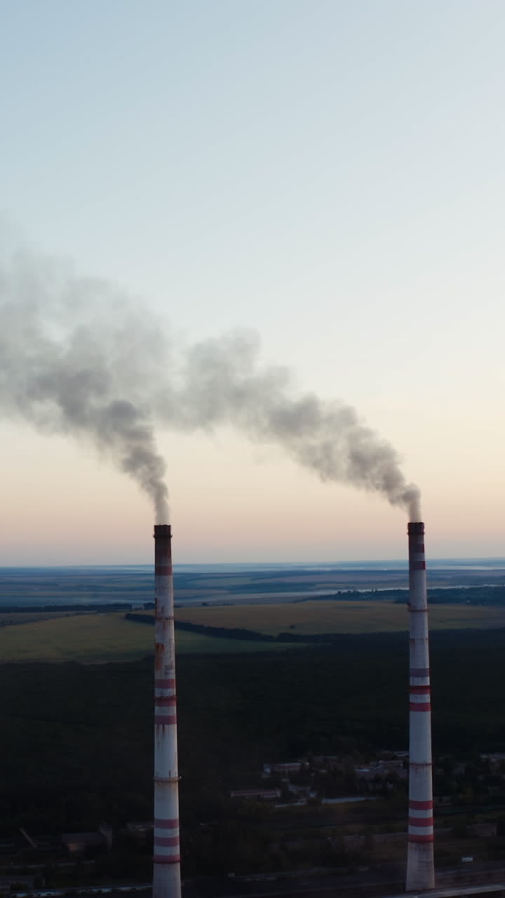 Two pipes with smoke on the beautiful landscape of nature. White smoke pouring out from industrial pipes in the air in the evening. Vertical video