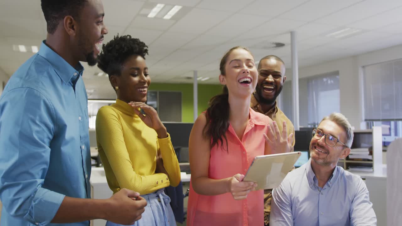 Happy diverse male and female business colleagues using tablet and talking in office