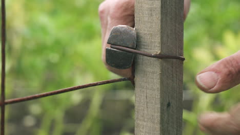 mano de un hombre adulto usando pinzas de acero apretando la valla alambrada en el patio