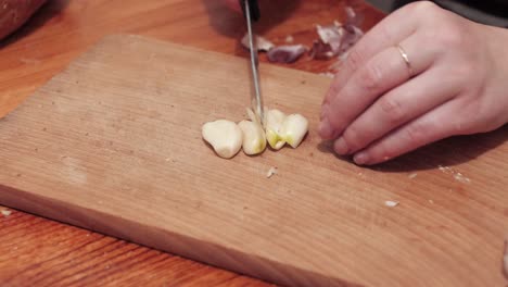 woman's hands with a knife chops the first clove of garlic on a chopping board