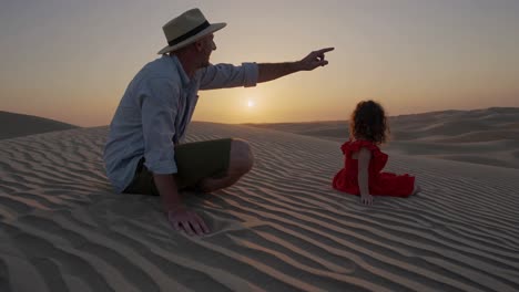 father and daughter watching sunset in the desert