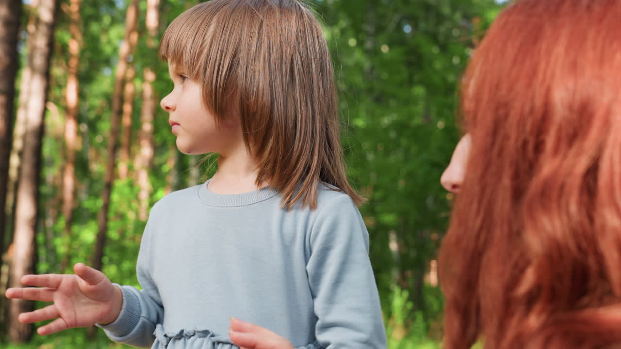 Bright eyed girl attentively listens to mother during warm outdoor conversation, showing curiosity, innocence, and emotional bond, surrounded by forest greenery and natural sunlight creating peaceful