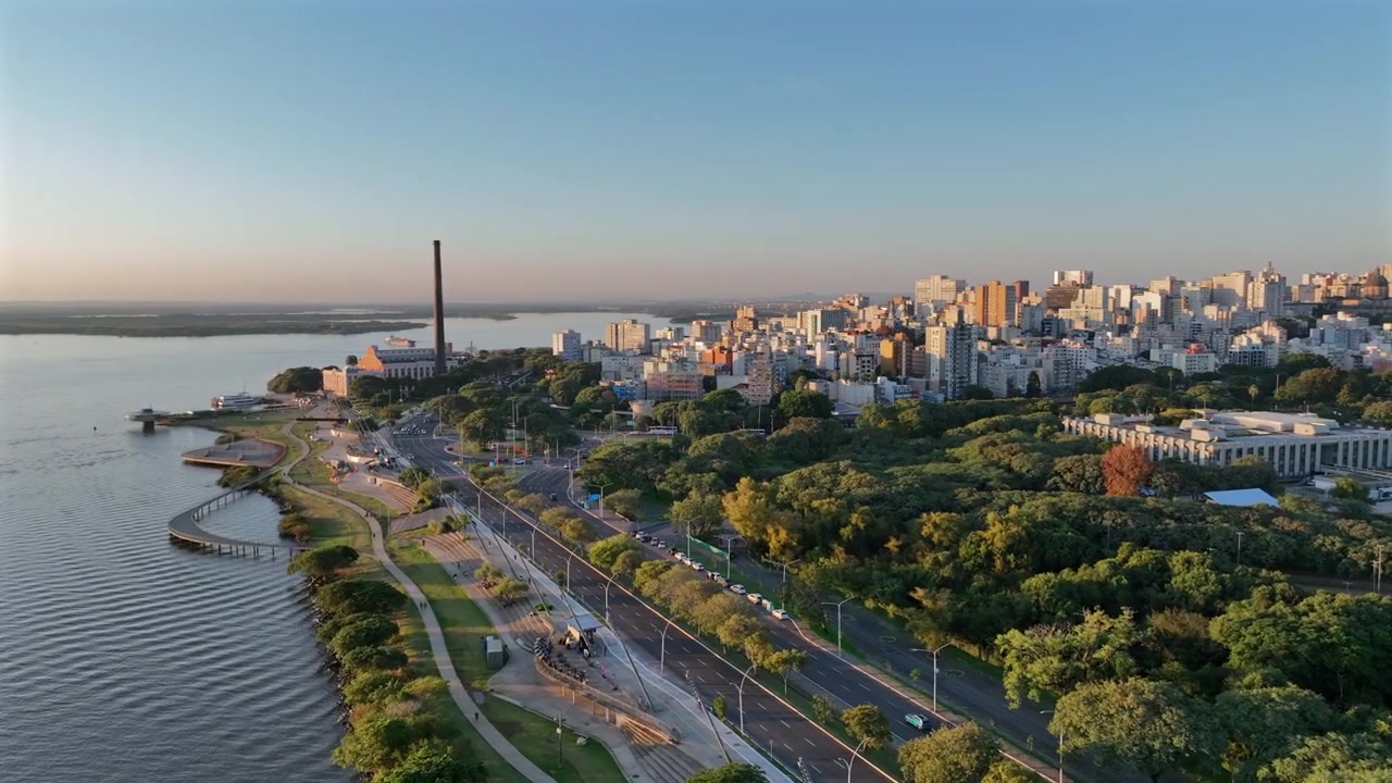 Strada lungomare di Porto Alegre con parco verde e skyline cittadino sullo sfondo, e una prospettiva dinamica all'ora d'oro.