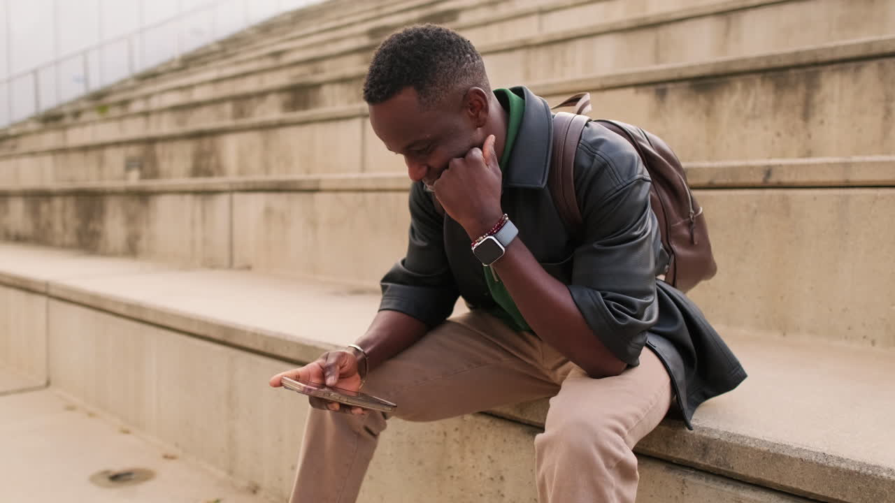 Smiling African American Man Sitting on Steps Using Smartphone