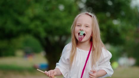 funny little girl eats candyfloss outdoors. portrait of adorable child holds a colorful cotton candy and eating joyfully in the park in summer day.