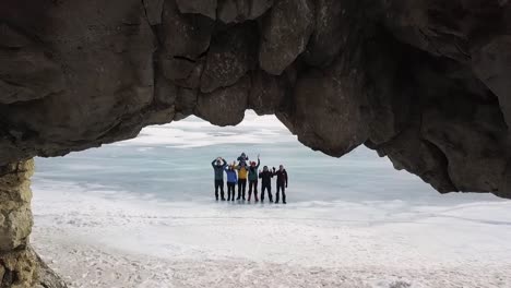 personas de pie bajo un arco de roca frente a un lago congelado