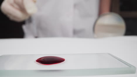 diapositiva con gota de sangre y mujer con pipeta y lupa