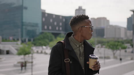 young trendy african american man portrait student texting browsing social media using smartphone drinking coffee beverage in busy city people walking urban lifestyle