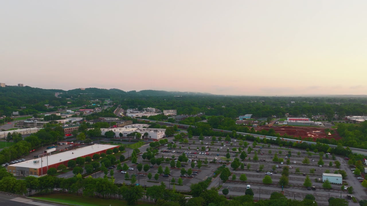 Panoramic aerial view of suburbs Birmingham Alabama featuring industrial buildings, parking lots, and a railway line surrounded by lush greenery under a soft morning sky.