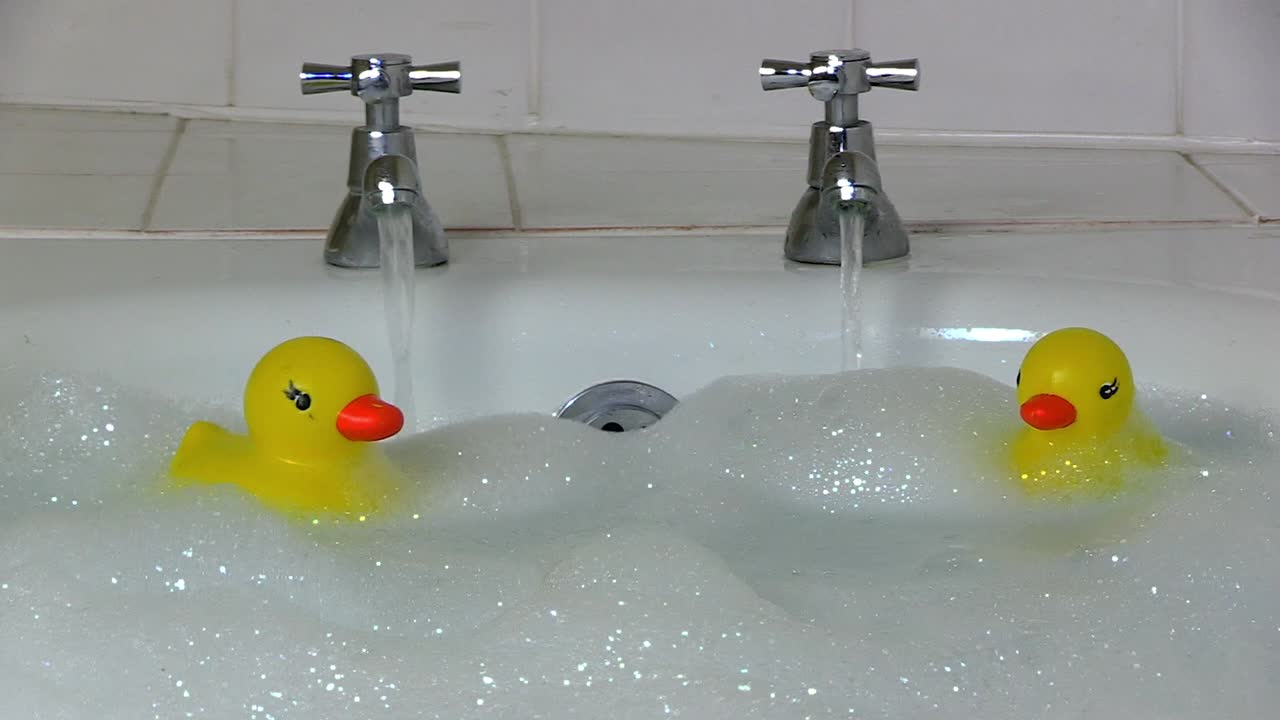 Two plastic ducks bob up  and down in a sparkly bubble bath.