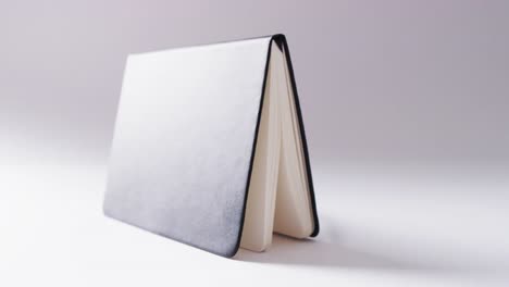 Close-up-of-open-black-book-standing-horizontal-with-copy-space-on-white-background-in-slow-motion