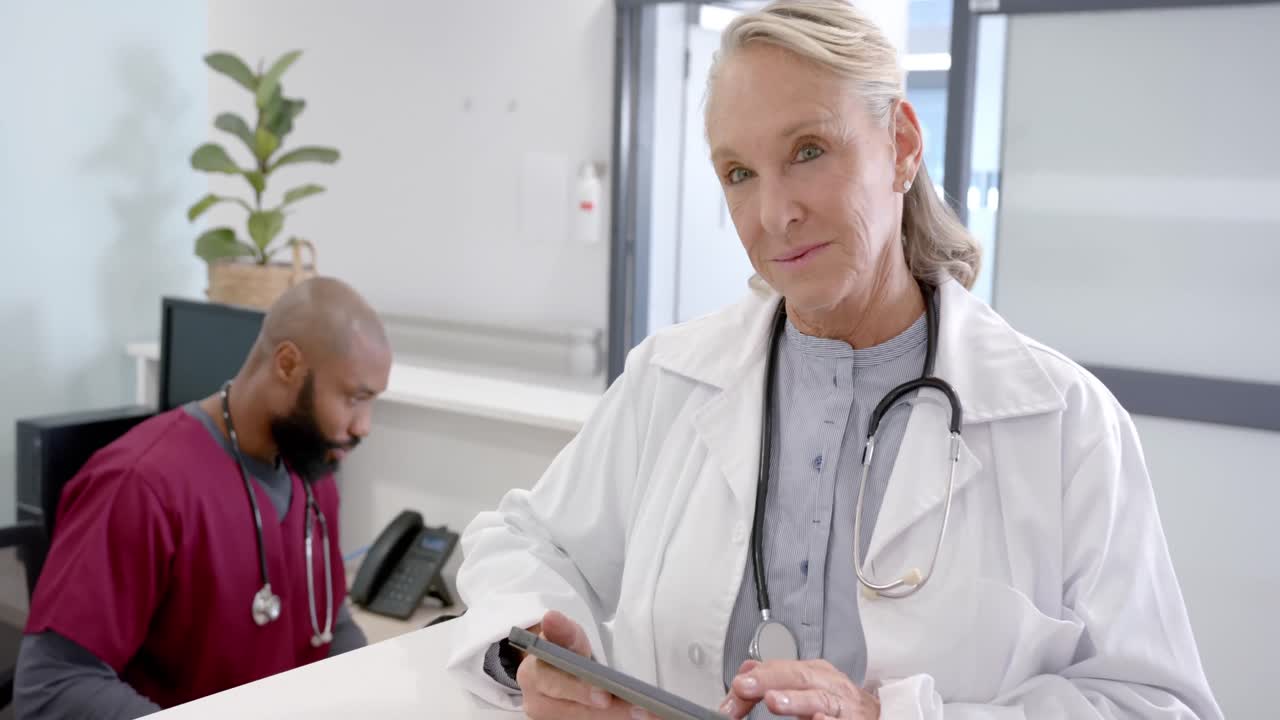 Ritratto di dottoressa anziana caucasica felice che usa un tablet nella reception dell'ospedale, al rallentatore.