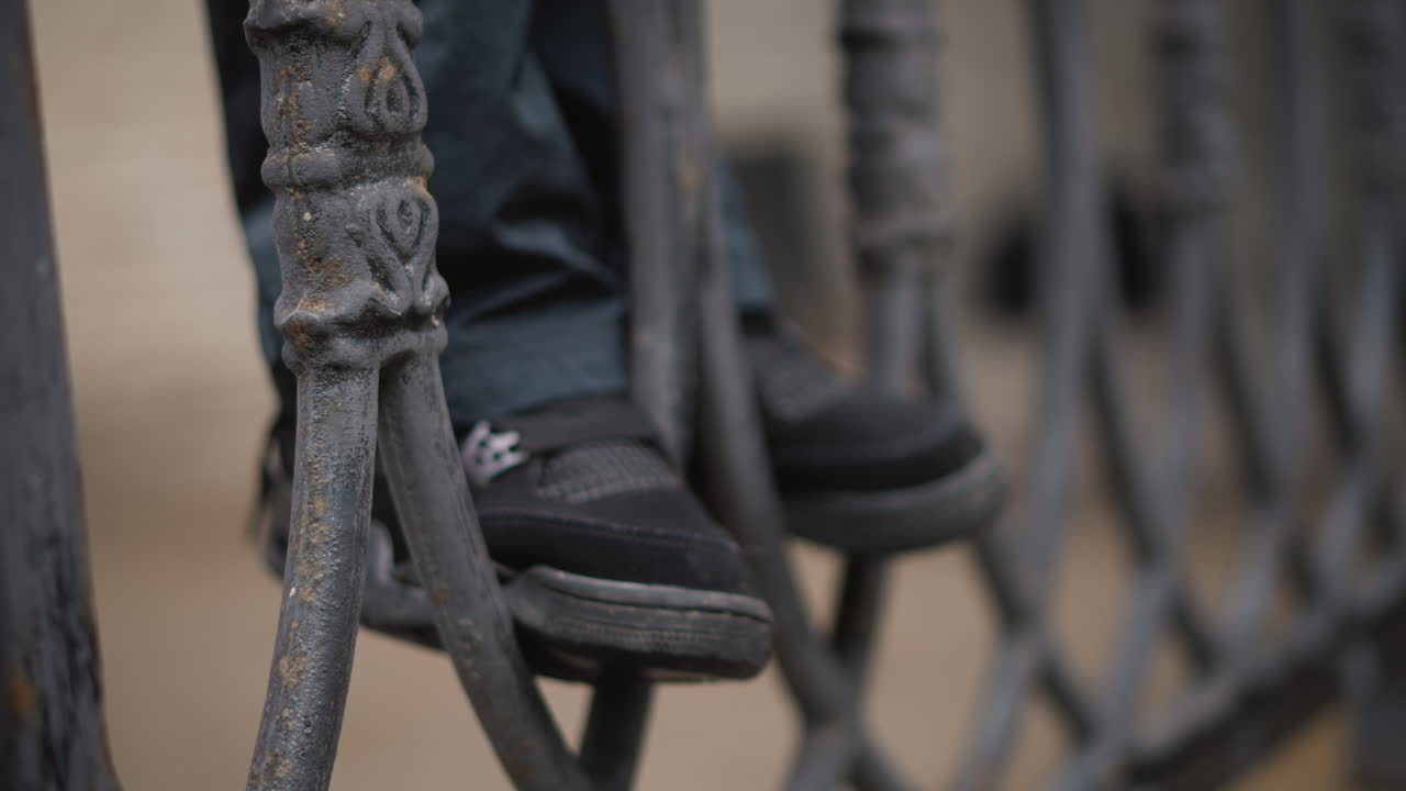 Donna attraversa con cautela una recinzione decorativa. Donna manovra con attenzione una recinzione in ferro ornata in una mattina di pioggia in città. Navigare attraverso intricate barriere metalliche su strade bagnate durante il tragitto urbano mattutino.