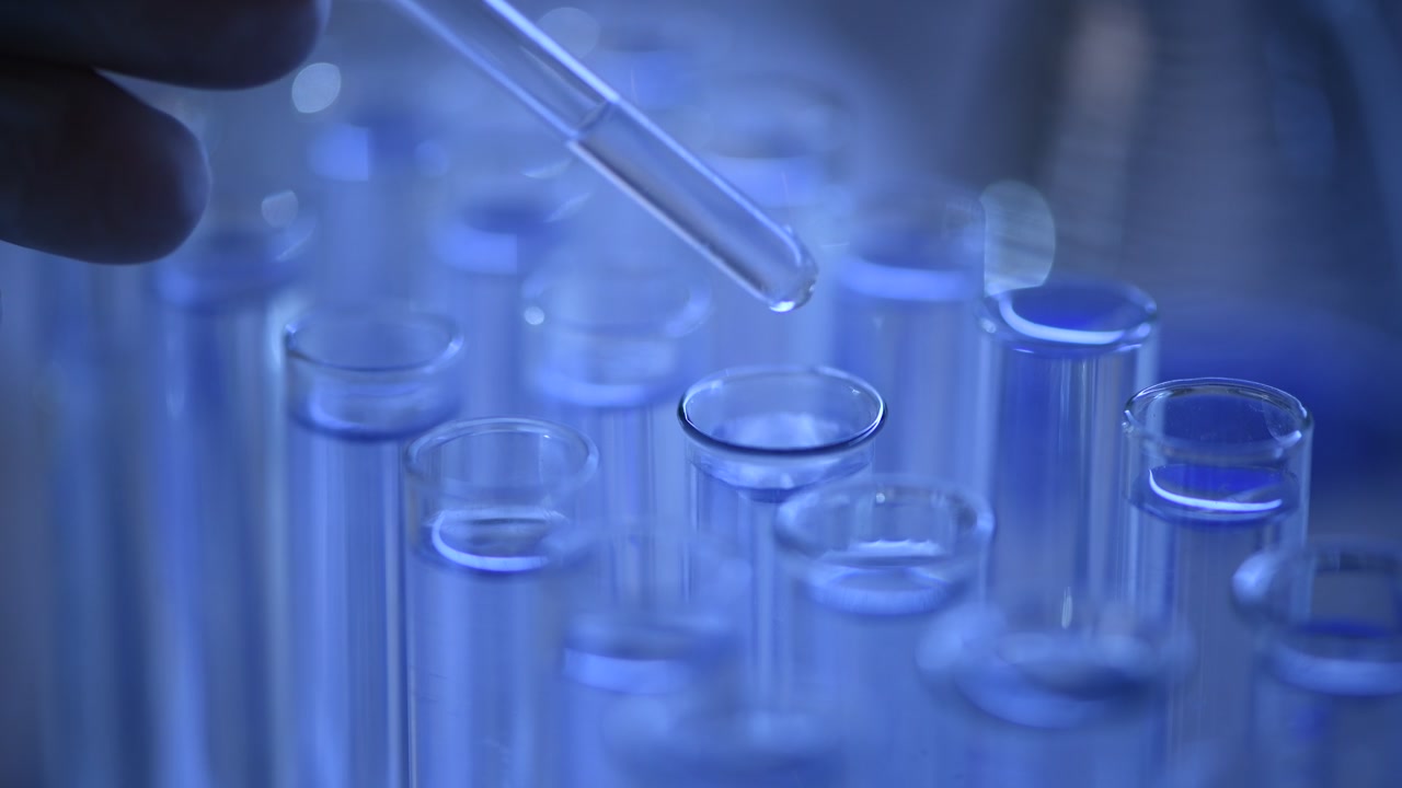 Close-up of Pipette Dropping Liquid into Test Tube in Blue Laboratory