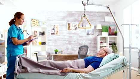 nurse checking on old and sick patient lying in hospital bed