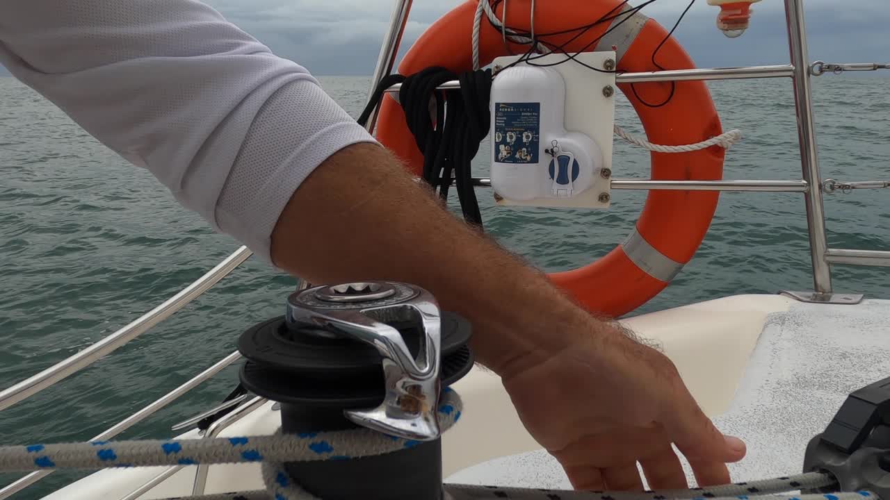 Tightening a rope around a winch on a sailboat close to a lifebuoy