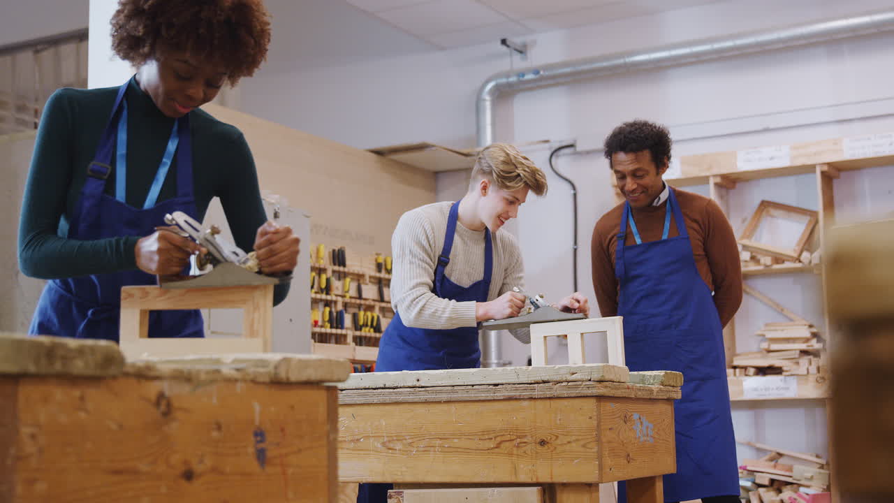 Tutor With Carpentry Student In Workshop Studying For Apprenticeship At College Using Wood Plane