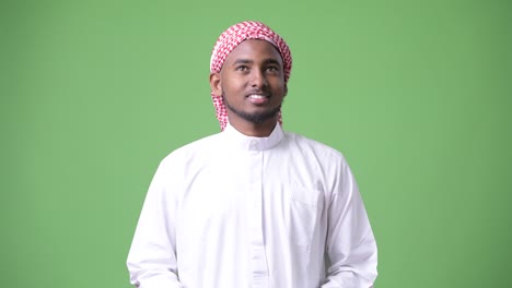 young handsome african man wearing traditional muslim clothes against green background