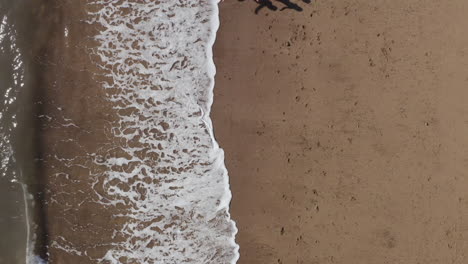 Drohnenaufnahme-Einer-Familie-Im-Urlaub,-Die-Am-Strand-Entlang-Läuft-Und-Wellen-Bricht