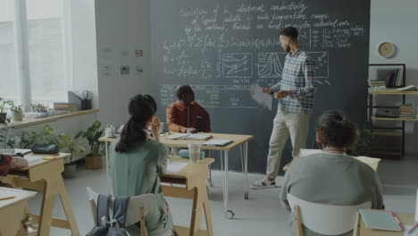 teacher explaining scientific formulas on a blackboard to students in a classroom